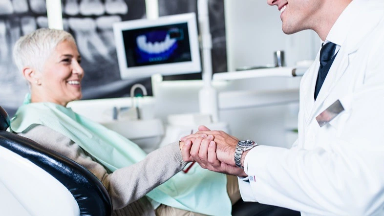 Patientin auf Praxissitz, die Hand des Zahnarzts schüttelt
