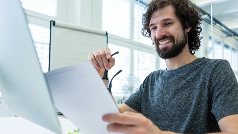 Lächelnder Mann prüft Unterlagen am Schreibtisch – Power-Workshop zahntechnische Abrechnung Fortgeschrittene | Spitta Akademie