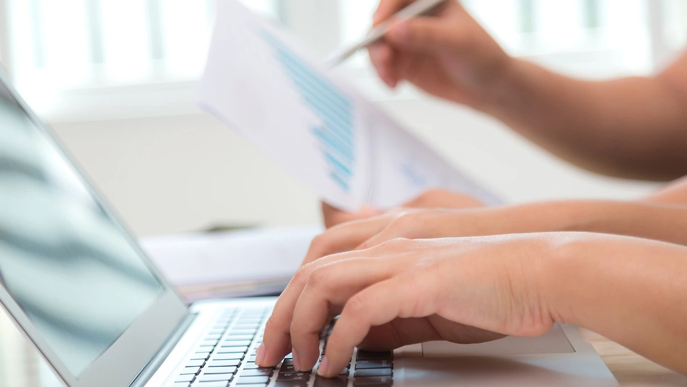 Hände tippen auf Laptop und halten Dokument mit Stift – Online-Kurs EBZ technische Anbindung und praktische Anwendung | Spitta Akademie