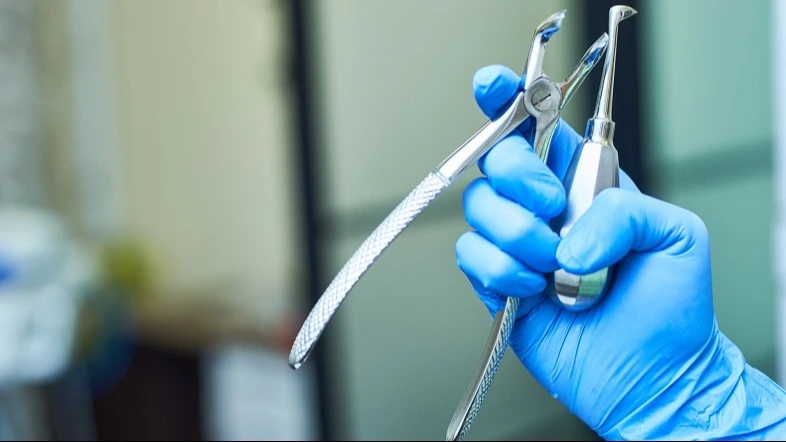 Hand mit blauem Latexhandschuh hält chirurgische Zahnextraktionszange – Online-Seminar Abrechnung chirurgischer Leistungen für Einsteiger | Spitta Akademie