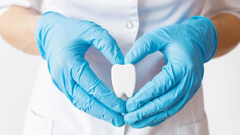 Hände mit blauen Handschuhen formen Herz um Zahnmodell – Webinar-Aufzeichnung Hygienemanagement 10 Tipps für die Zahnarztpraxis | Spitta Akademie