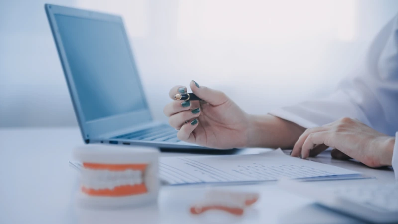 Zahntechnikerin arbeitet am Laptop mit Zahnmodell auf dem Schreibtisch – Webinar-Aufzeichnung BEB kalkulieren zahntechnische Abrechnung | Spitta Akademie