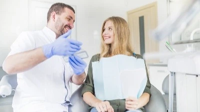 Zahnarzt erklärt lächelnder Patientin Behandlung im Behandlungsstuhl – Webinar-Aufzeichnung Perspektivwechsel Patientenkommunikation Zahnarztpraxis | Spitta Akademie