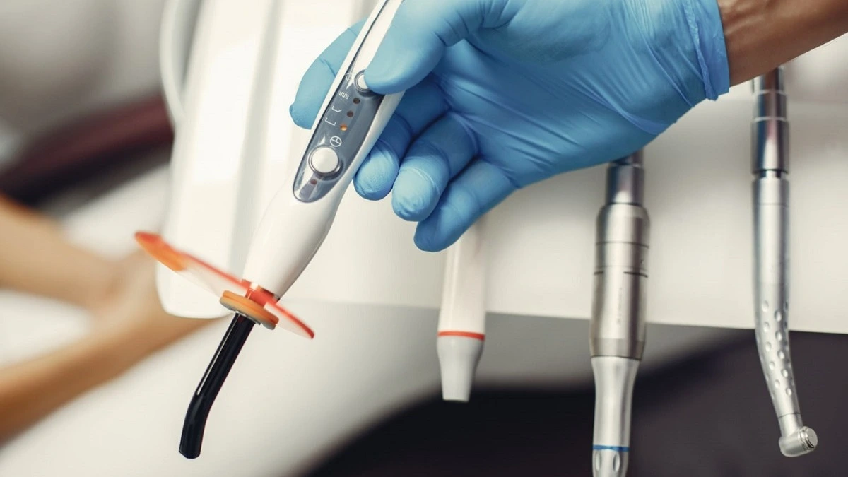 Hand mit blauem Handschuh hält zahnärztliche Polymerisationslampe und Instrumente – Online-Kurs Auswirkungen Amalgamverbot BEMA-Nr. 13 | Spitta Akademie